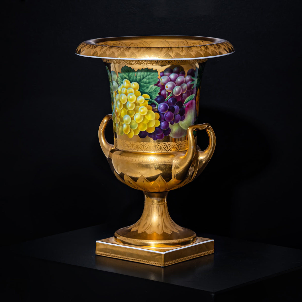 Decorative urn with gold accents and fruit design on a black background