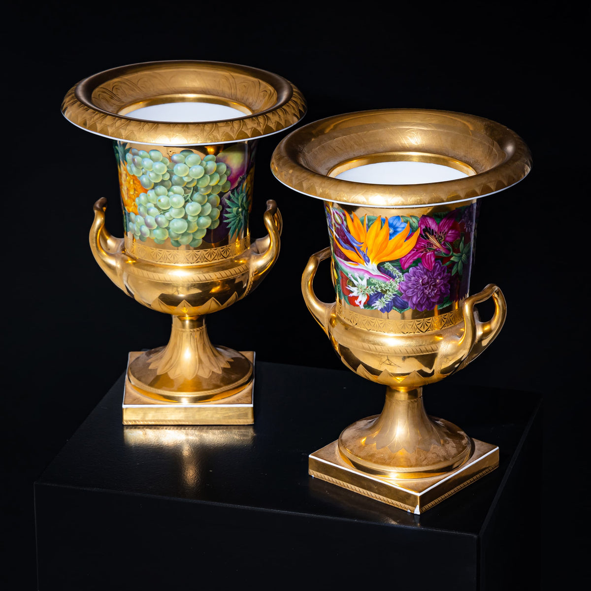 Two ornate gold urns with colorful designs on a black background