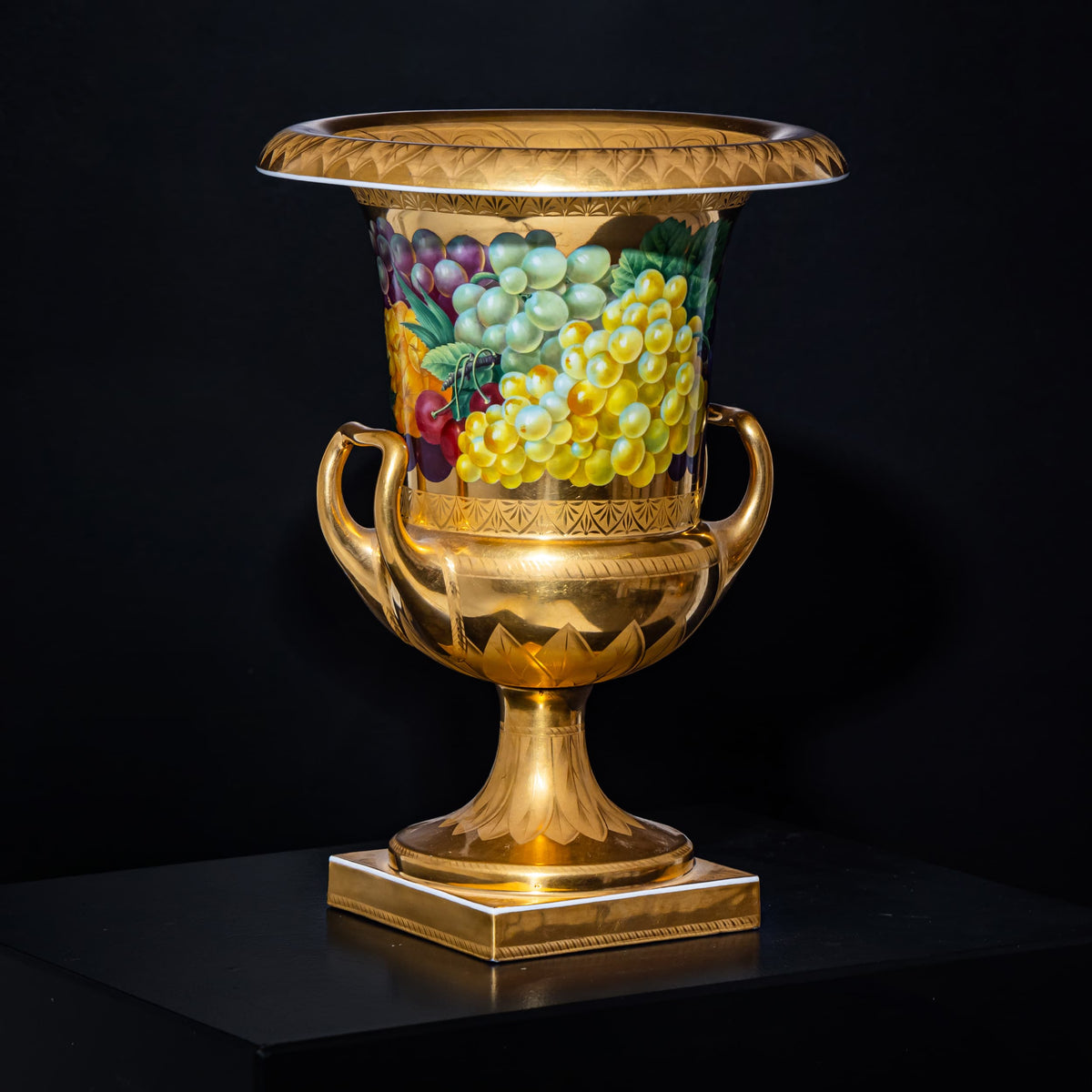 Decorative urn with gold finish and fruit design on a black background